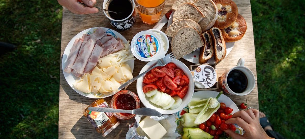 Enjoy a delightful outdoor brunch with bread, cheese, cold cuts, coffee, and fresh vegetables.