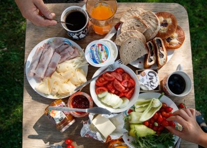 Enjoy a delightful outdoor brunch with bread, cheese, cold cuts, coffee, and fresh vegetables.