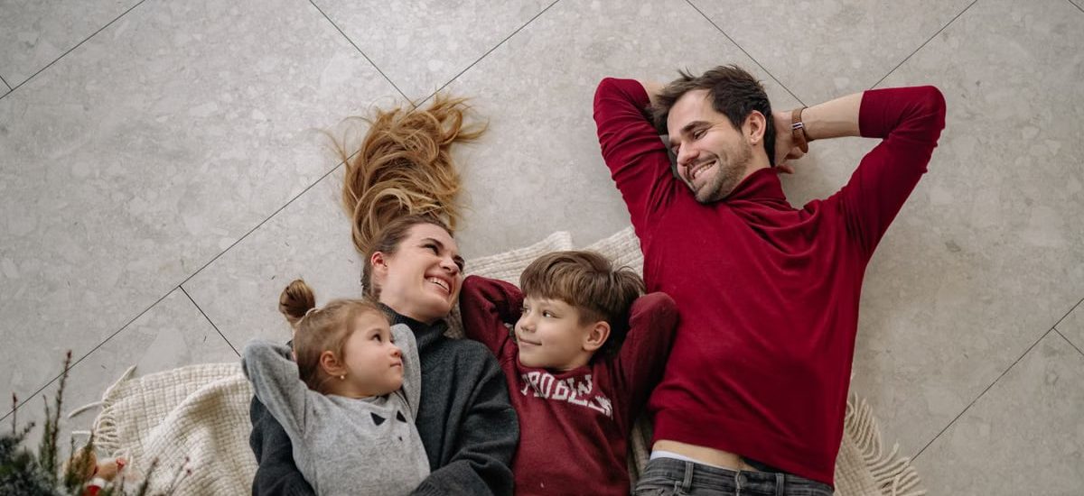 Smiling family of four lying on a blanket, sharing happiness and love indoors.