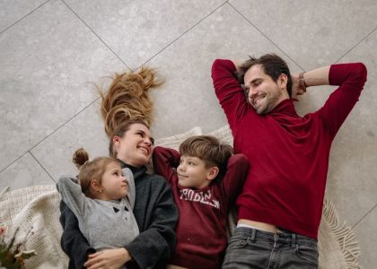 Smiling family of four lying on a blanket, sharing happiness and love indoors.