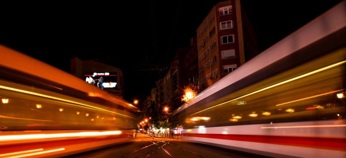 Twin trains speed past each other at night in a vibrant urban setting, creating a dynamic city atmosphere.